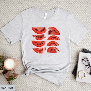A beautiful, rustic print of eight red ripe tomato slices. Design is multi-color on a Athletic Heather Grey Bella+Canvas 3001 t-shirt. Garment is displayed flat with two books, stylish glasses, candle and decorative eucalyptus branch.