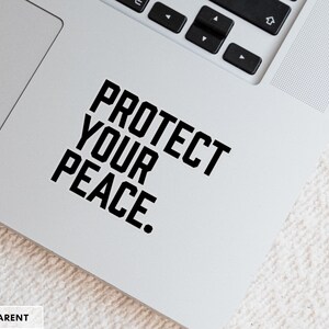 A bold typographic design reading PROTECT YOUR PEACE. Design is printed on a kiss-cut vinyl sticker with a transparent border. Sticker is shown on an open silver laptop, next to the track pad.