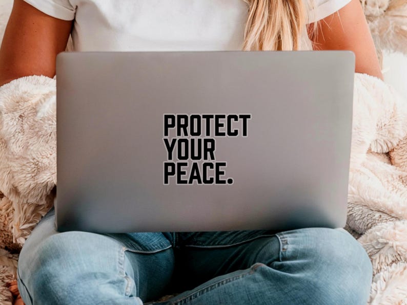 A bold typographic design reading PROTECT YOUR PEACE. Design is printed on a kiss-cut vinyl sticker with a white border. Sticker is shown on the back of an open silver laptop as a young lady is working.