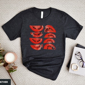 A beautiful, rustic print of eight red ripe tomato slices. Design is multi-color on a Dark Heather Grey Bella+Canvas 3001 t-shirt. Garment is displayed flat with two books, stylish glasses, candle and decorative eucalyptus branch.