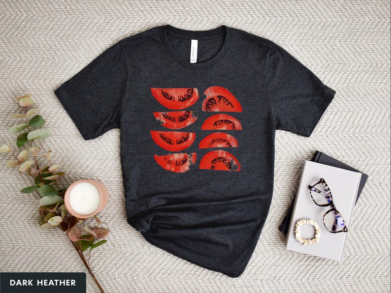 A beautiful, rustic print of eight red ripe tomato slices. Design is multi-color on a Dark Heather Grey Bella+Canvas 3001 t-shirt. Garment is displayed flat with two books, stylish glasses, candle and decorative eucalyptus branch.