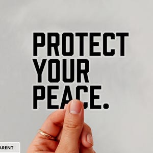 A bold typographic design reading PROTECT YOUR PEACE. Design is printed on a kiss-cut vinyl sticker with a transparent border. Sticker is being held by a single hand on a neutral, light grey background.