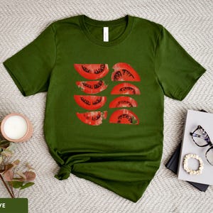 A beautiful, rustic print of eight red ripe tomato slices. Design is multi-color on a Olive Bella+Canvas 3001 t-shirt. Garment is displayed flat with two books, stylish glasses, candle and decorative eucalyptus branch.