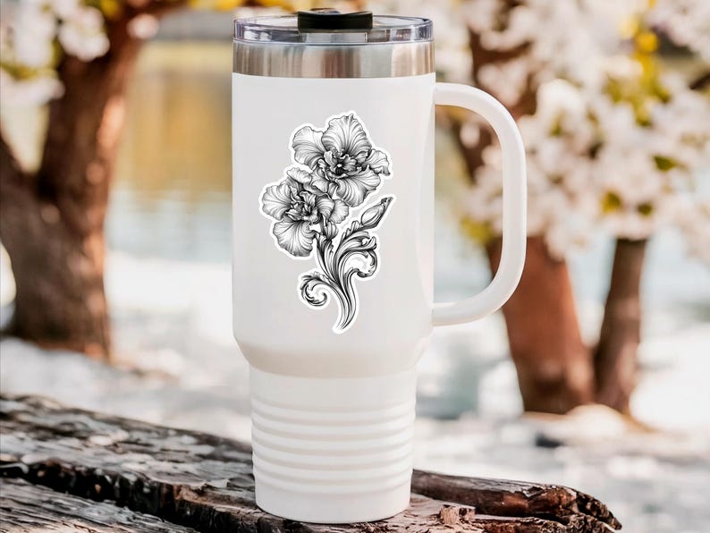 An ornate engraved style rendering of two orchids with elegant flourishes in a balanced, elegant arrangement. Design is printed on a kiss-cut vinyl sticker with a white border. Sticker is shown on a tall white tumbler in a luxurious outdoor setting.