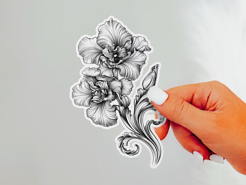 An ornate engraved style rendering of two orchids with elegant flourishes in a balanced, elegant arrangement. Design is printed on a kiss-cut vinyl sticker with a white border. Sticker is being held by a single hand on a neutral, light grey background.