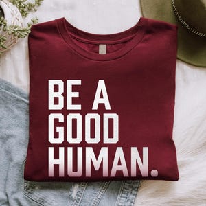 May include: A maroon t-shirt with white text that reads "BE A GOOD HUMAN."