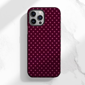 Puede incluir: Una funda para smartphone con un fondo burdeos oscuro y un patrón de pequeños lunares rosas espaciados uniformemente. La funda tiene un borde oscuro y recortes para la cámara y otras funciones.