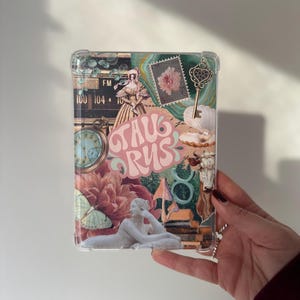 May include: A clear phone case with a collage of vintage images, including a woman in a dress, a clock, a flower, a key, and a bull. The text "TAURUS" is written in pink letters.