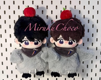May include: Two plush dolls with black and brown hair, each topped with a red apple. They have large eyes, gray fur bodies, and wear gray scarves. The dolls are displayed against a white pegboard background.