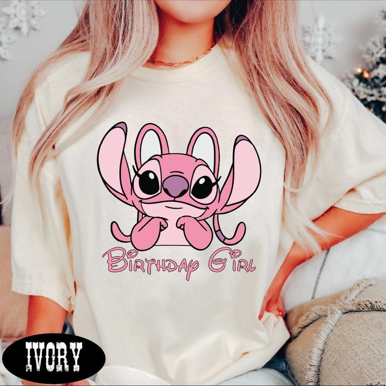 A woman wearing a white t-shirt with a pink cartoon character and the text "Birthday Girl" printed on it.