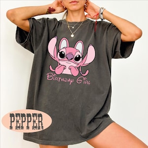 A person wearing a gray t-shirt with a pink cartoon character and the text "Birthday Girl" printed on it.