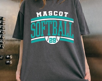 May include: Dark gray t-shirt with the words "MASCOT SOFTBALL" in white and teal lettering. A teal and white design arches above and below the word "SOFTBALL". A baseball with the number "29" is below the word "SOFTBALL".
