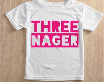 May include: White t-shirt with a crew neck and short sleeves. The shirt features the words "THREE NAGER" in bright pink block letters, with the word "NAGER" inside a pink rectangle.