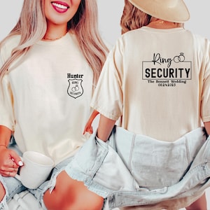 May include: Cream-colored t-shirts with black text and graphics. One shirt reads "Hunter RING SECURITY" on the front. The other shirt reads "Ring SECURITY The Bennett Wedding 08.24.2025" on the back. The shirts are worn with denim shorts.