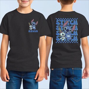 A black t-shirt with a graphic design featuring a character from the movie "Stitch". The character is shown in a playful pose, surrounded by a checkered pattern. The t-shirt also has the name "Kevin" printed on the front.