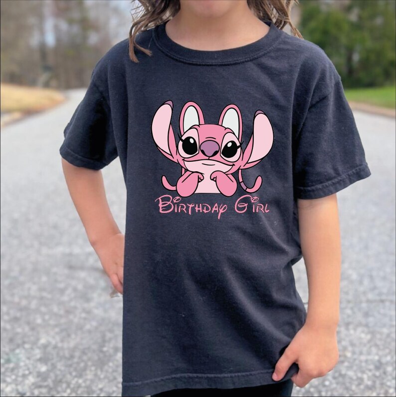 A person wearing a black t-shirt with a pink cartoon character and the text "Birthday Girl" printed on it.
