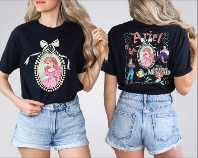 A woman wearing a black t-shirt with a graphic of Ariel from The Little Mermaid and denim shorts.