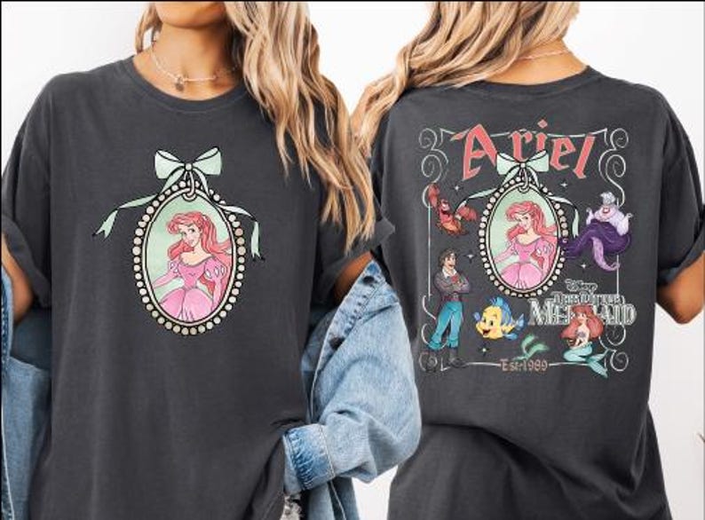 two t-shirts with the character Ariel from the Disney animated film "The Little Mermaid". The t-shirt on the left has a portrait of Ariel and the text "Ariel" above her, while the t-shirt on the right has a graphic of Ariel surrounded by various sea creatures and the text "Ariel" and "The Little Mermaid" on the back.