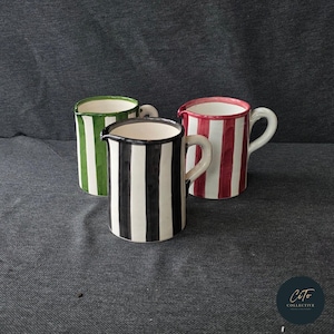 Könnte beinhalten: Drei Keramikkrüge mit gestreiften Designs. Die Krüge sind grün, rot und schwarz-weiß.