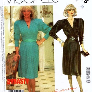 Könnte beinhalten: McCall's Schnittmuster 2215 mit zwei Kleiderdesigns. Ein Kleid ist türkis mit V-Ausschnitt, plissiertem Rock und passendem Gürtel. Das andere Kleid ist schwarz mit V-Ausschnitt, langen Ärmeln und einem dekorativen Gürtel. Der Schnitt enthält den Text "Dynasty TV Series Collection".