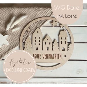 May include: A wooden round ornament with a cut-out design of a Christmas village with houses, trees, and stars. The ornament has the text "Frohe Weihnachten" (Merry Christmas) in German. The ornament is on a light brown surface.