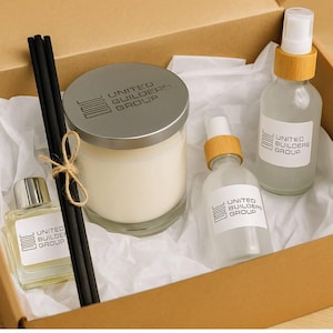 May include: A gift box containing a candle, diffuser, and spray bottles. The candle has a silver lid, and the bottles have bamboo accents. The box is filled with white tissue paper, and the products have labels with the text "UNITED BUILDERS GROUP".