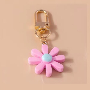 May include: A gold key chain with a pink flower charm. The flower has a light blue center.