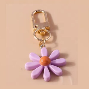 May include: A purple flower keychain with a gold metal clasp and ring. The flower has a yellow center.