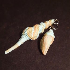May include: Two seashell earrings with a light blue and orange swirl pattern. The earrings are made of polymer clay and have a gold-colored hook.