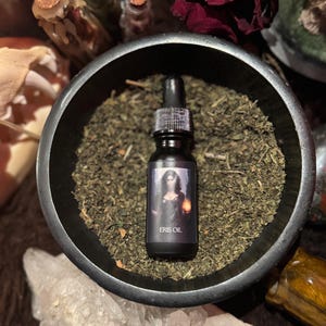 May include: A small glass bottle with a black dropper and a label that reads "Eris Oil". The bottle is sitting in a black bowl filled with dried herbs.