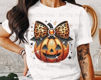 May include: A white t-shirt with a glittery orange pumpkin with a black jack-o'-lantern face. The pumpkin is topped with a large brown and orange leopard print bow with a sparkly jewel in the center.