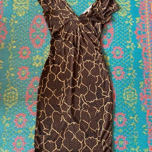 May include: A brown, knee-length dress with a V-neck and short sleeves. The dress features a repeating pattern of small brown circles and a network of tan lines, creating a textured appearance. The dress is made of a soft, stretchy material.