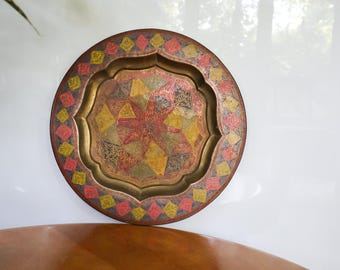 May include: A round, decorative tray with a gold, red, and yellow geometric pattern. The tray has a raised edge and a scalloped design.