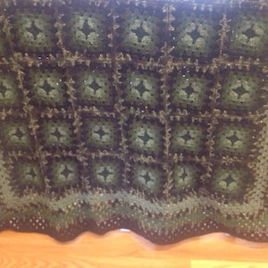 May include: A green and black crocheted blanket with a square pattern. The blanket has a fringed edge.