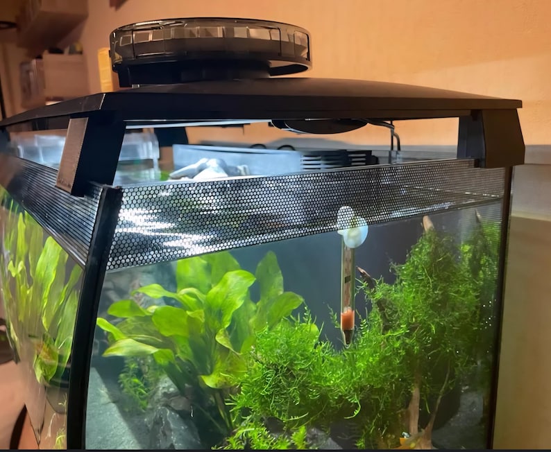 May include: A rectangular aquarium with a black frame and a built-in light fixture. The tank is filled with water, aquatic plants, and a thermometer. The front of the tank has a mesh screen. The aquarium is designed to house aquatic life.