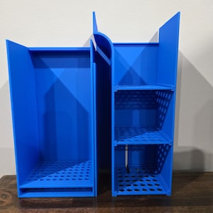 May include: Three blue plastic storage organisers with open shelves and a grid pattern on the bottom. The organisers are stacked on top of each other.