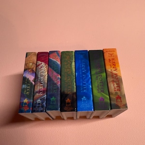 May include: A set of seven Harry Potter books, each with a different colored cover. The books are arranged in order from left to right, with the first book being "Harry Potter and the Sorcerer's Stone" and the last book being "Harry Potter and the Deathly Hallows".