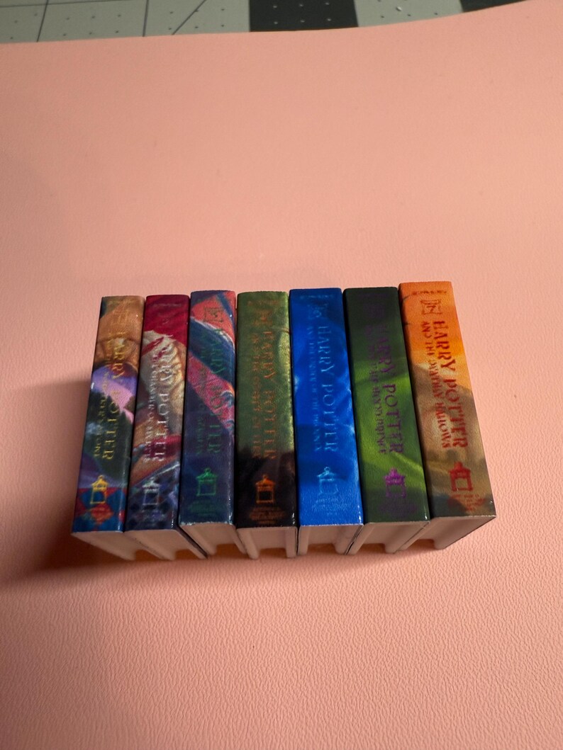 May include: A set of seven Harry Potter books, each with a different colored cover. The books are arranged in order from left to right, with the first book being "Harry Potter and the Sorcerer's Stone" and the last book being "Harry Potter and the Deathly Hallows".