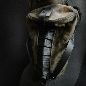 May include: A brown leather thigh holster with a black leather pouch and a black metal ring. The holster has a distressed look and is secured with a black strap.