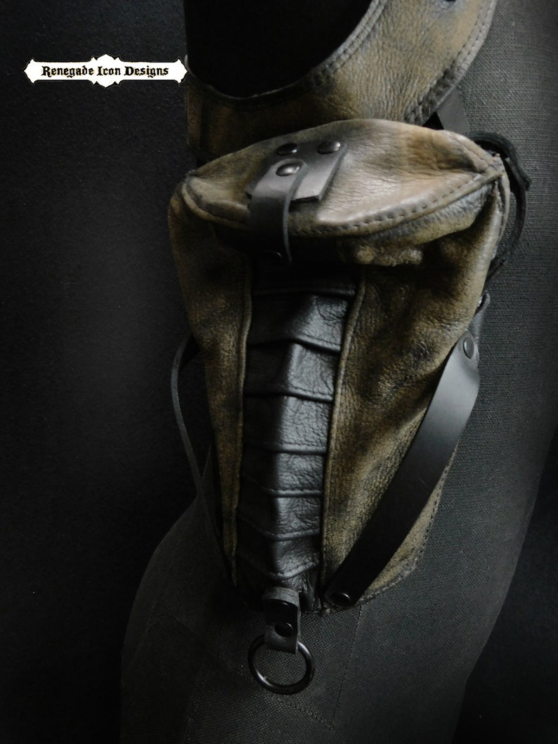May include: A brown leather thigh holster with a black leather pouch and a black metal ring. The holster has a distressed look and is secured with a black strap.