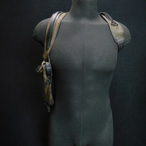 May include: A black leather holster with a brown strap and a metal buckle. The holster is worn on a mannequin's shoulder.