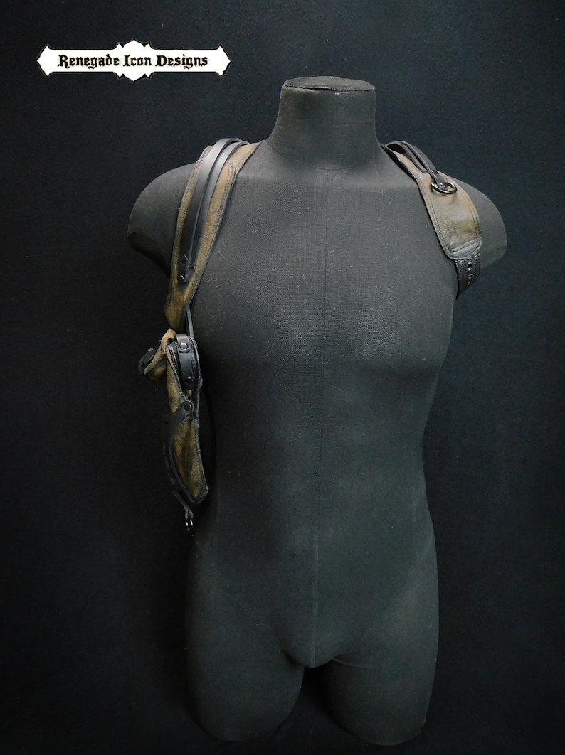 May include: A black leather holster with a brown strap and a metal buckle. The holster is worn on a mannequin's shoulder.