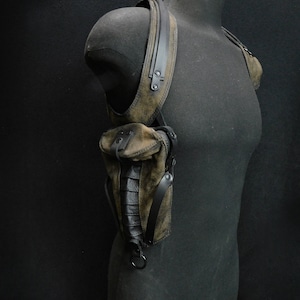 May include: A brown leather shoulder holster with black straps and buckles. The holster has a pouch on the front and a strap that goes around the shoulder.