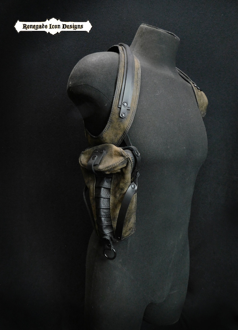 May include: A brown leather shoulder holster with black straps and buckles. The holster has a pouch on the front and a strap that goes around the shoulder.