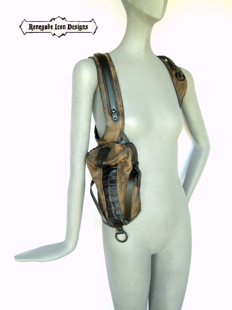May include: A brown leather shoulder bag with black accents and a metal ring. The bag has a flap with a buckle closure and a zippered pocket on the front. The bag is worn on a mannequin.