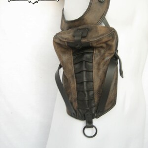 May include: A brown leather shoulder bag with black accents and a metal ring. The bag has a flap closure and a strap that goes over the shoulder.