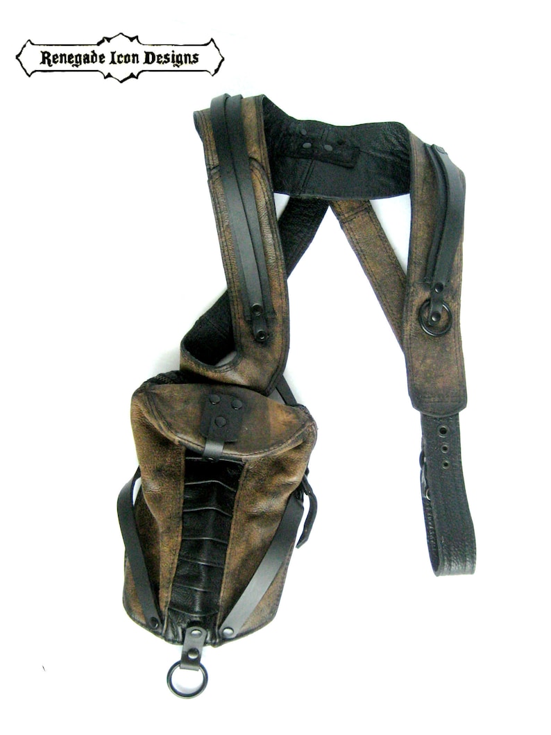 May include: A brown leather shoulder bag with black straps and a metal ring. The bag has a flap closure and a zippered pocket on the front. Renegade Icon Designs is printed on a black banner.