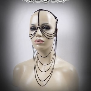 May include: A dark metal face and head chain with multiple strands of chain cascading down. The headpiece is attached to a black leather band. The text "Renegade Icon Designs" is above the headpiece.