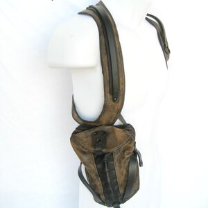 May include: A brown leather shoulder bag with black accents and a metal ring. The bag is worn on a mannequin's shoulder.