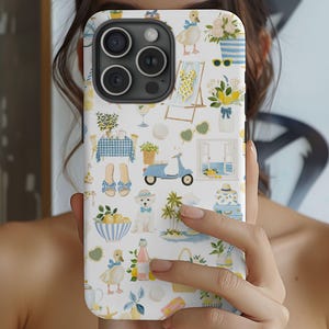 May include: A white iPhone case with a whimsical pattern of ducks, lemons, beach chairs, and a blue scooter. The case has a light blue border and a camera cutout. The design is in shades of yellow, blue, and white.